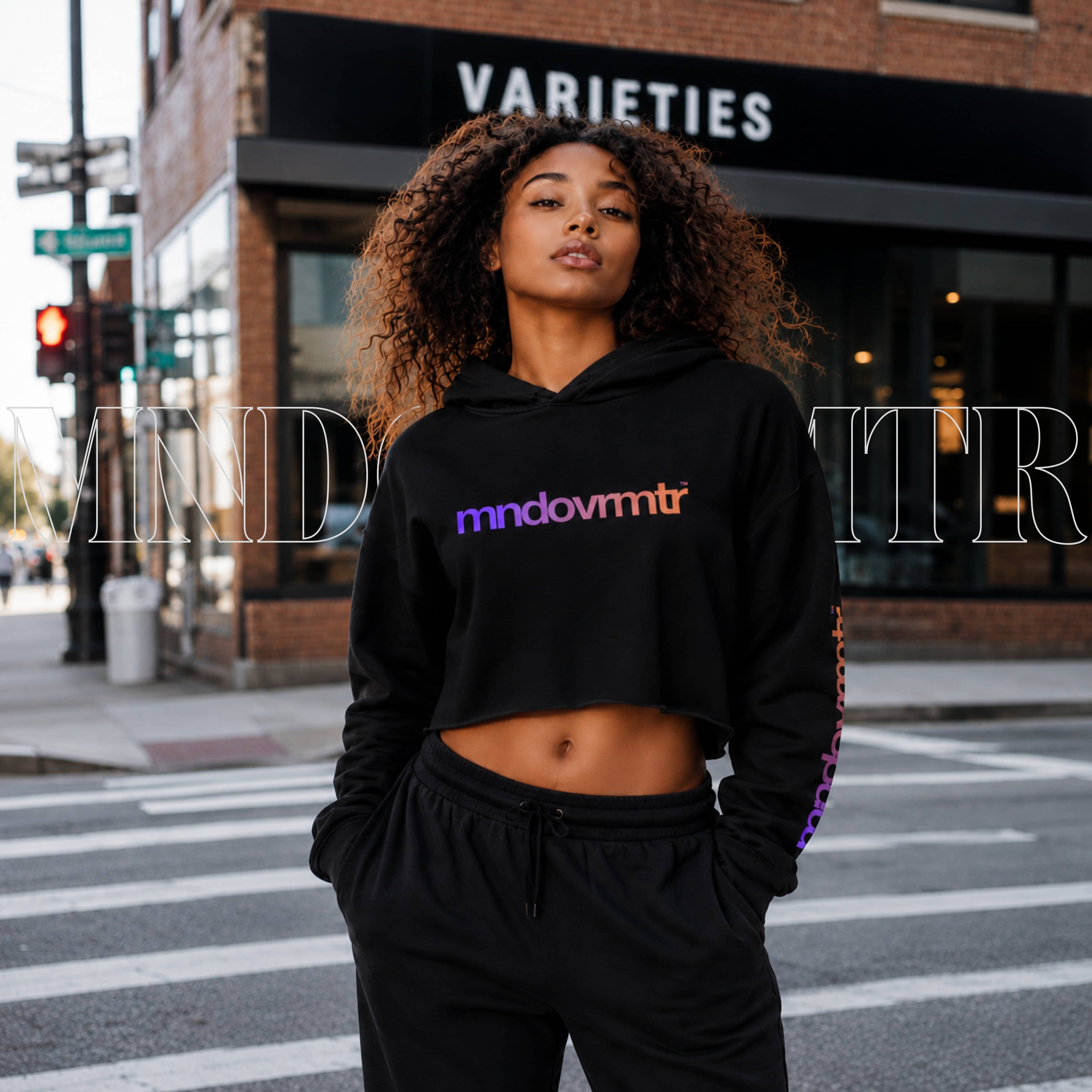 A stunning woman, wearing a black, raw hem, crop hoodie with a gradient 'mndovrmtr' text across the chest