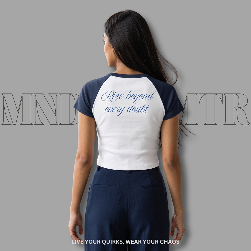 Woman wearing a white and blue crop baseball shirt with 'Rise beyond every doubt' text, against a gray background.
