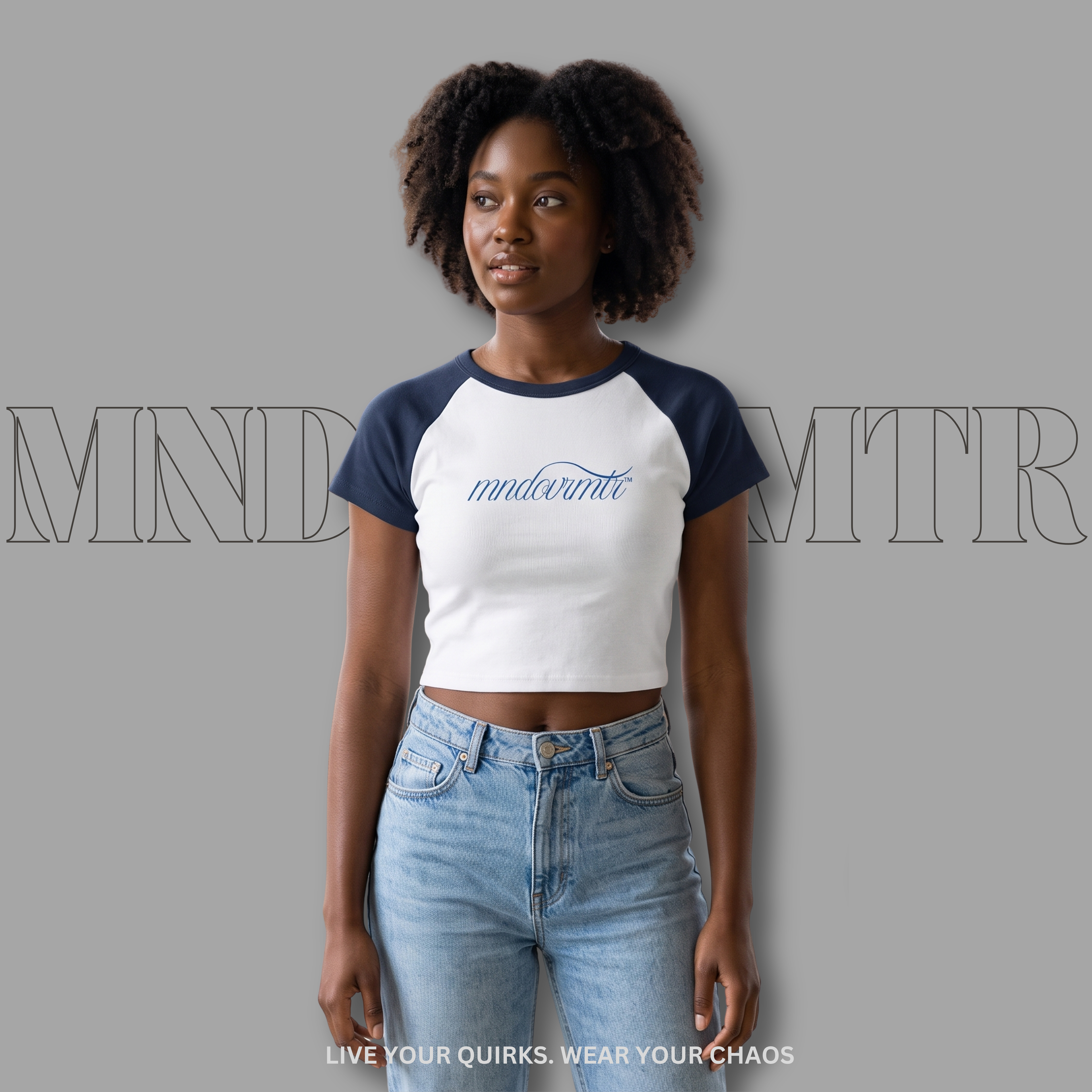 Woman wearing a white and blue crop baseball shirt with 'mndovrmtr™' text, against a gray background.