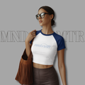 Woman wearing a white and blue baseball shirt with 'mndovrmtr™' text, holding a brown bag against a gray background.