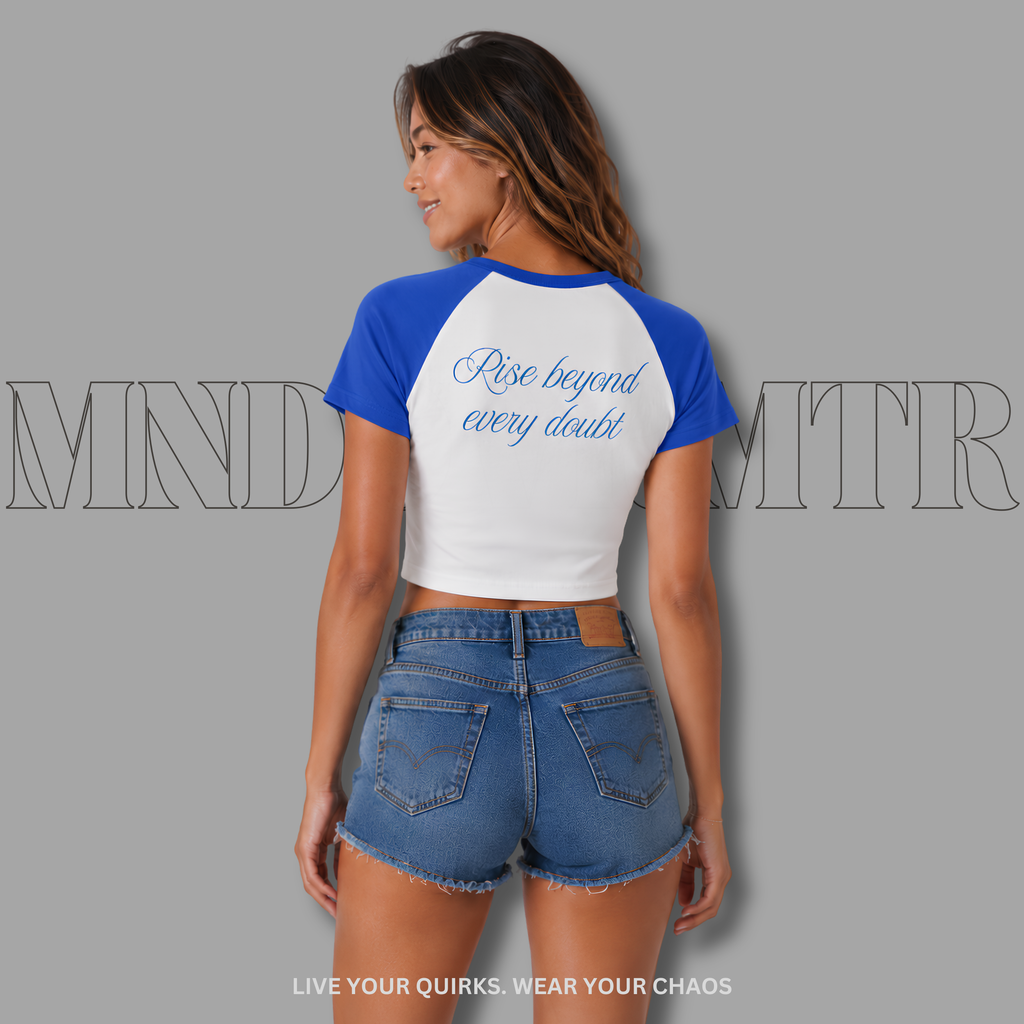 Woman wearing a white and royal blue crop baseball shirt with 'Rise beyond every doubt' text, against a gray background.
