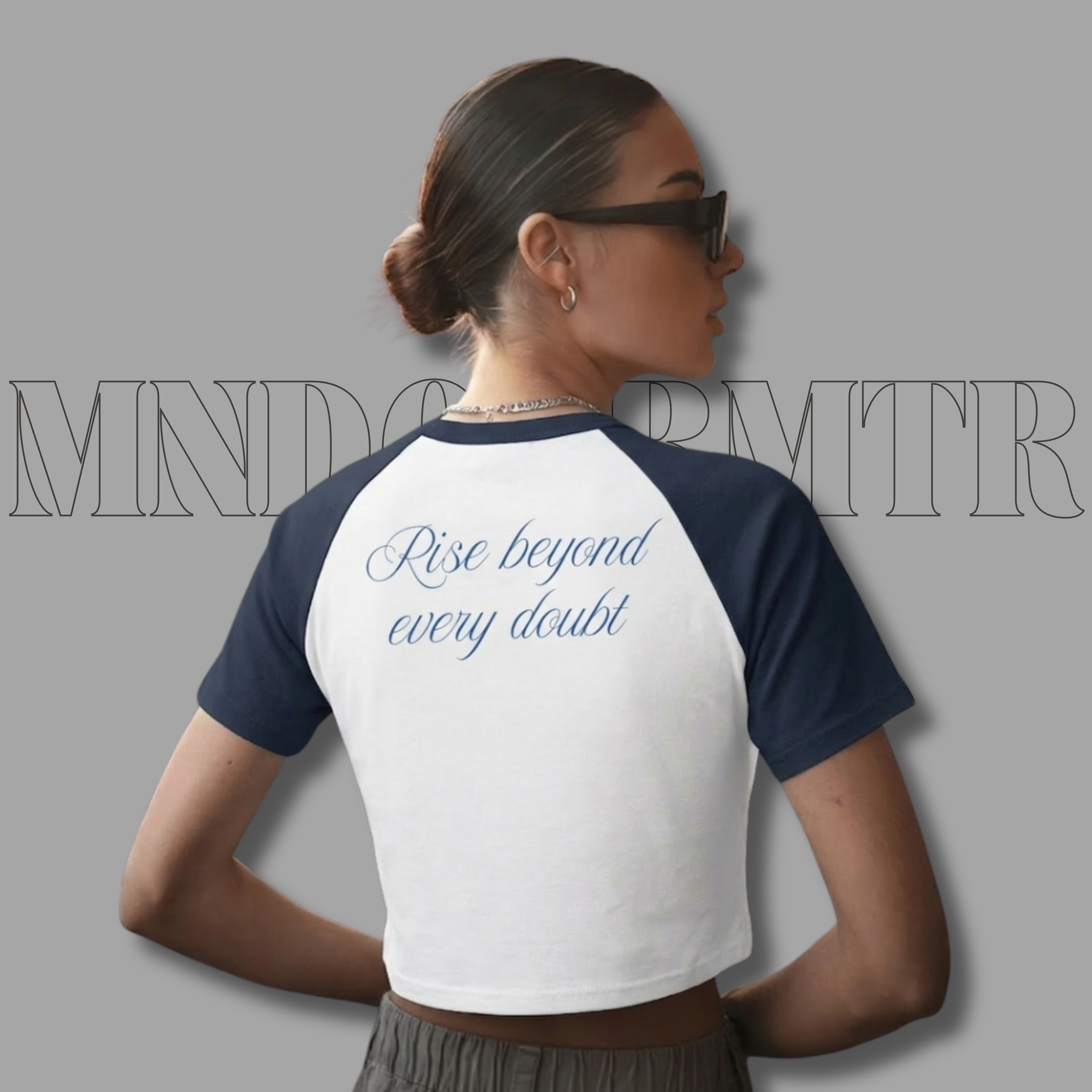 Person wearing a white and navy blue baseball shirt with text on the back, standing against a gray background.