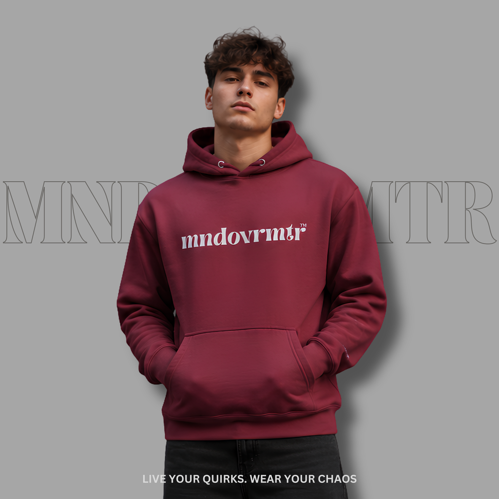 A good looking man wearing a maroon, fleece, pullover hoodie with 'mndovmrtr' printed in gray across the chest, posed against a solid gray background with a faint brand logo watermark.
