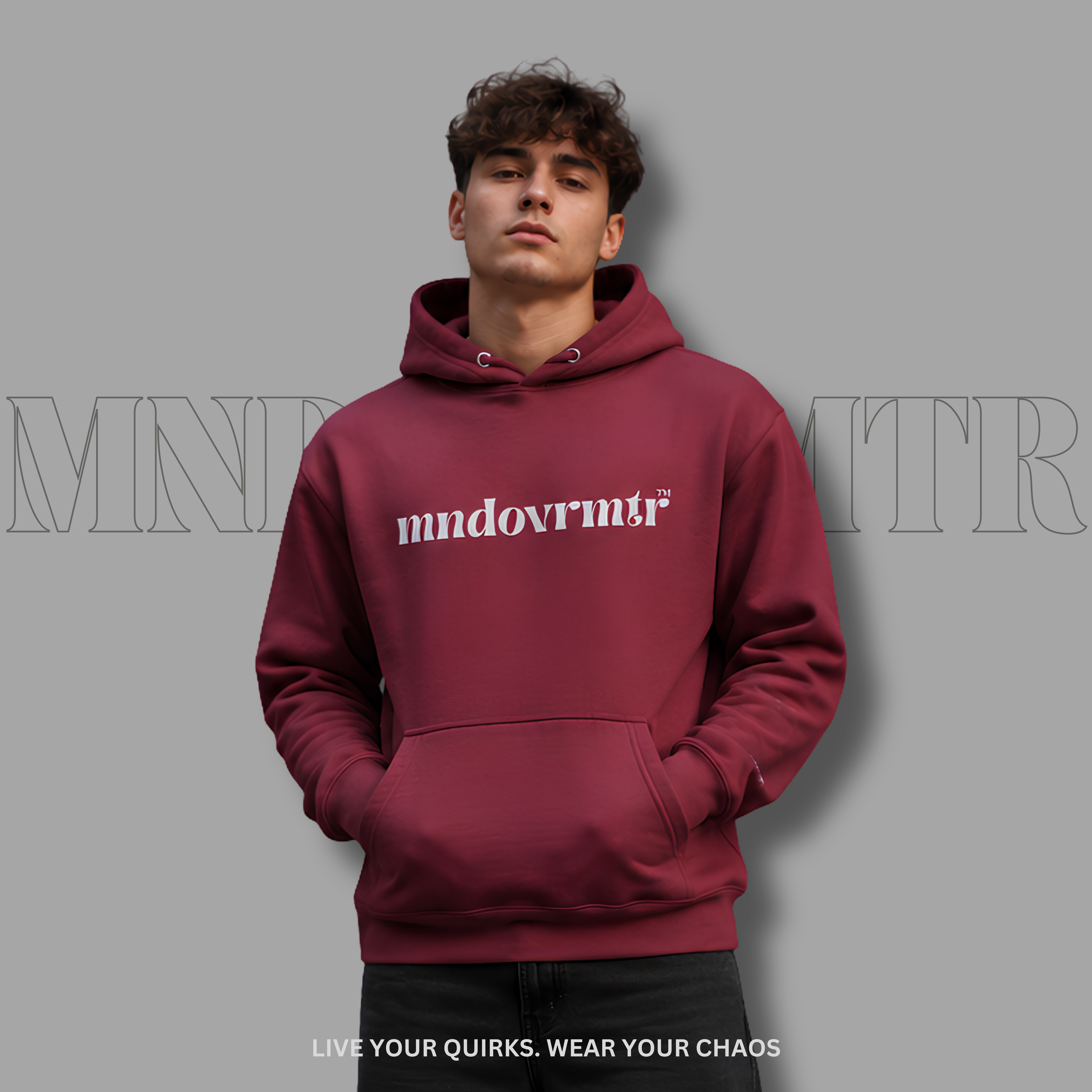 A good looking man wearing a maroon, fleece, pullover hoodie with 'mndovmrtr' printed in gray across the chest, posed against a solid gray background with a faint brand logo watermark.