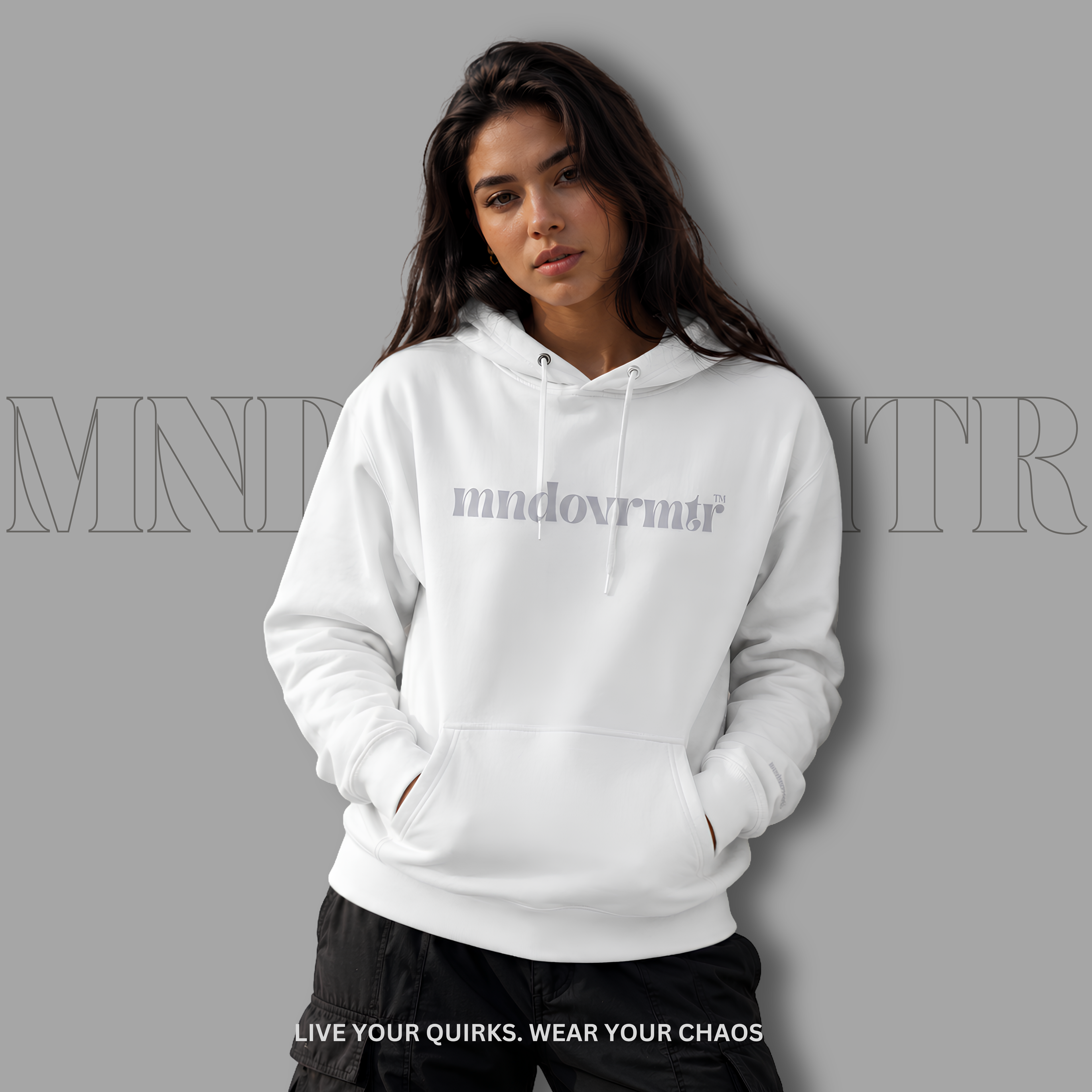 A pretty woman wearing a white, fleece, cotton, oversized, pullover hoodie with a gray 'mndovrmtr' logo on the chest, posed against a solid gray background with a faint brand watermark.