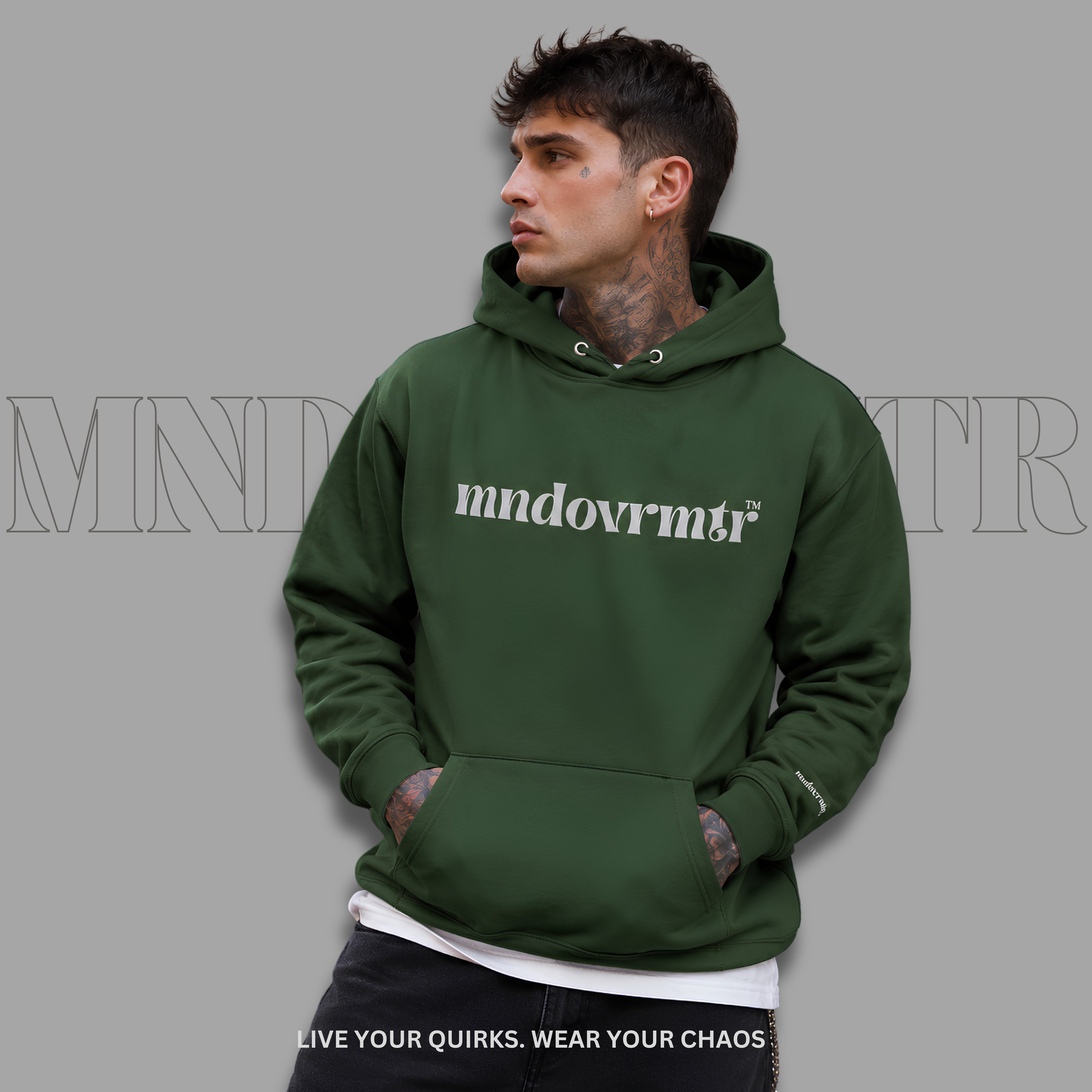 A man wearing an forest green pullover hoodie with the word 'mndovrmtr' printed in gray across the chest, posed against a solid gray background.