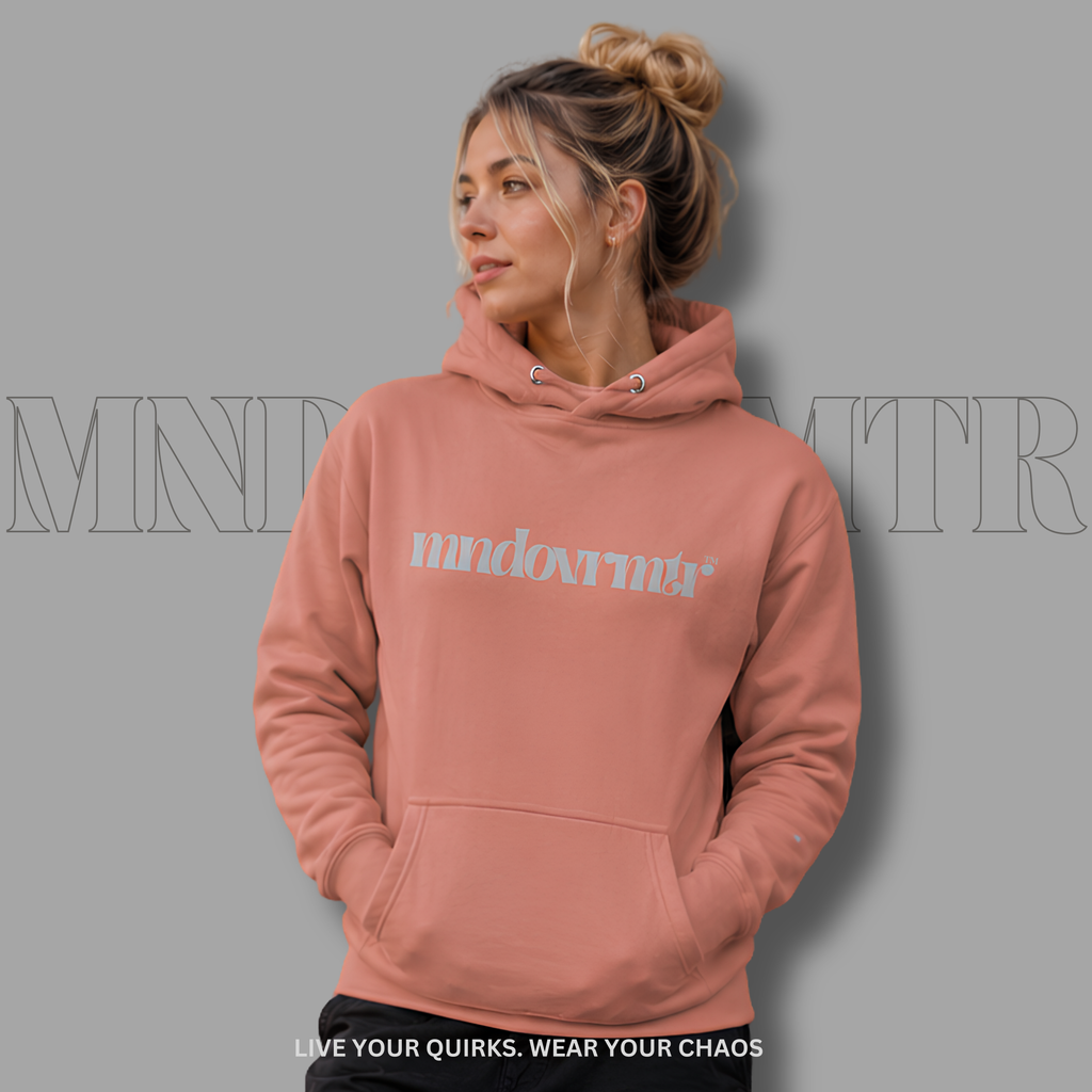 A woman wearing a dusty rose pink, oversized, fleece, cotton, hoodie with a gray "mndovrmtr" text on the chest, posed against a solid gray background with a faint brand watermark.