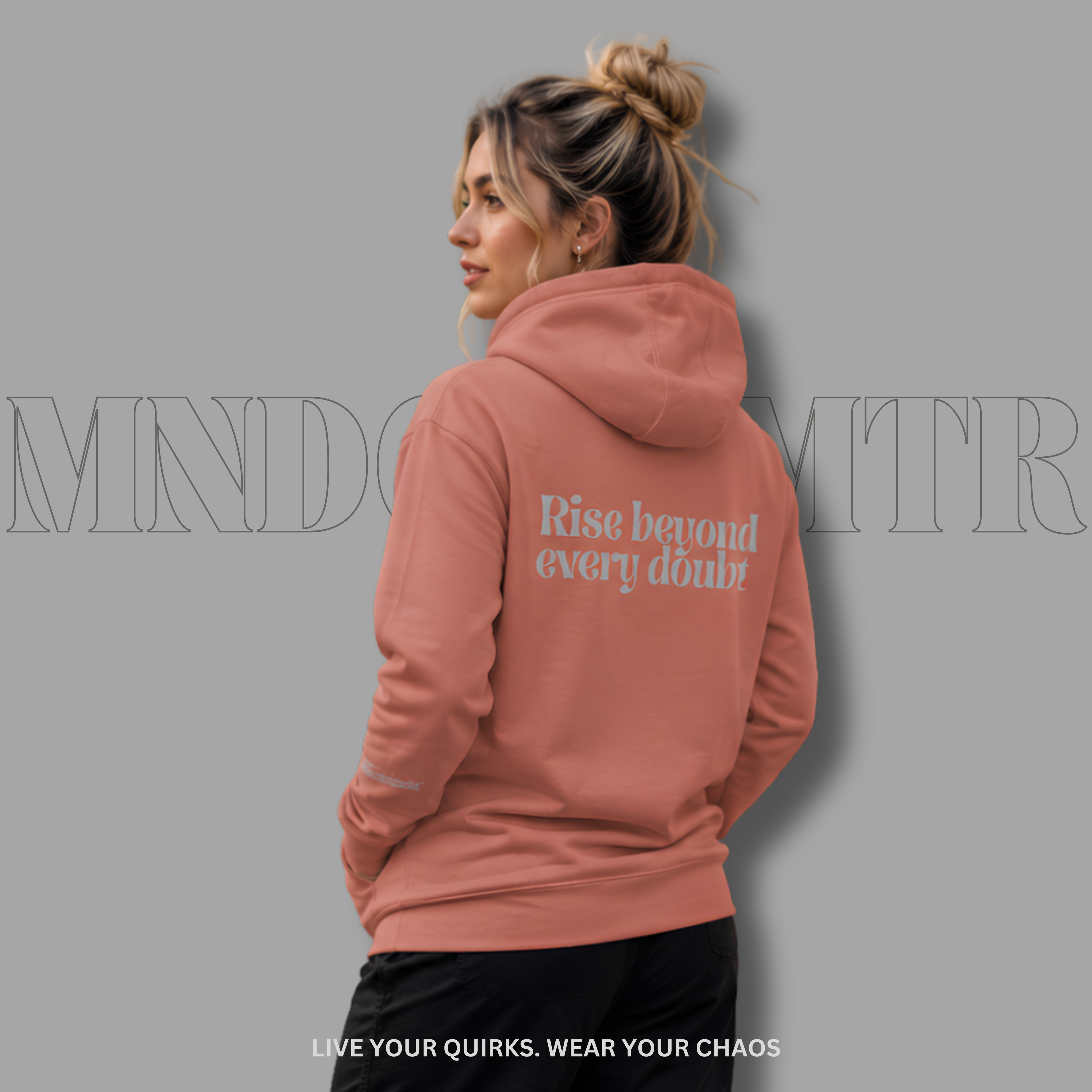 A woman shown from the back wearing a dusty rose, oversized, fleece, cotton, hoodie with the text 'Rise beyond every doubt' printed in light gray on the back, against a solid gray background.